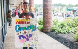 A young boy holding a happy community day sign he made