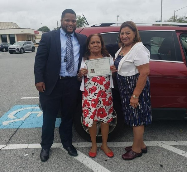 Three people standing together, the woman in the middle holding her citizenship certificate