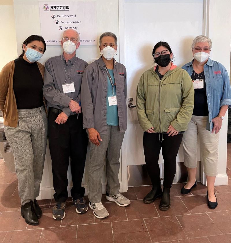 Five of the tax assisters, wearing face masks, but smiling behind them, as they pose together.