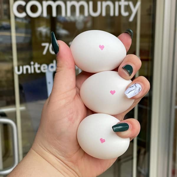 Three eggs with little hearts stamped on them are held in a women's hand in front of a door.