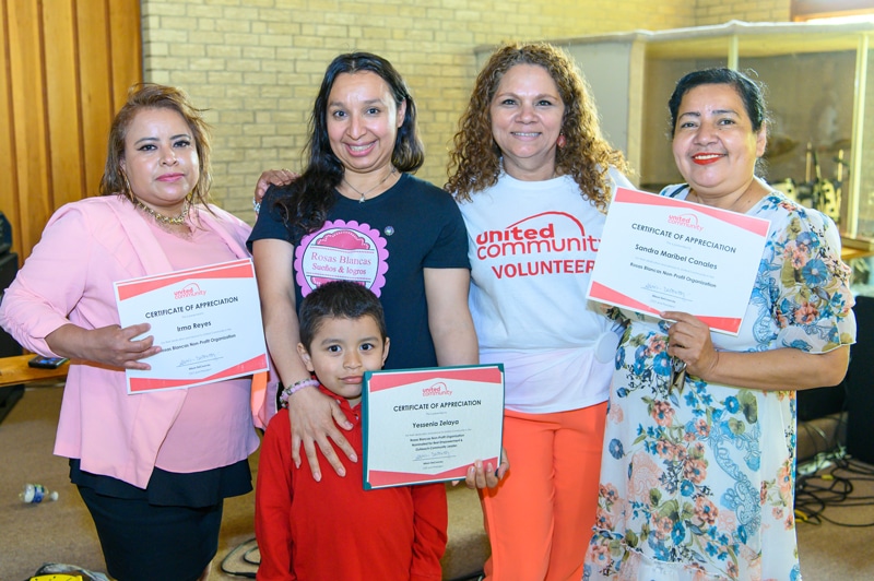 Four woman smiling and holding their volunteer certificates. One of their young sons is featured in the photo.