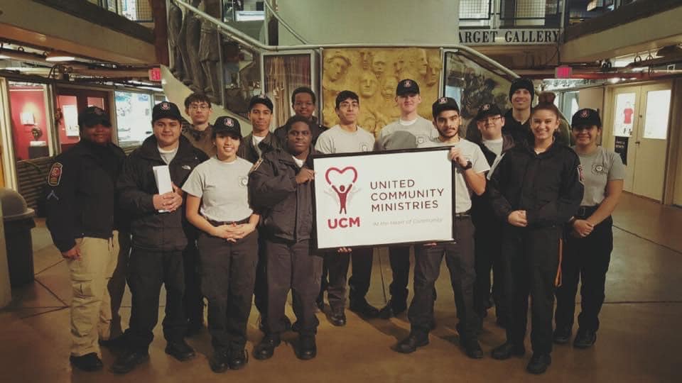 Group of teenagers from the Safety Cadet program holding a banner with the old United Community logo
