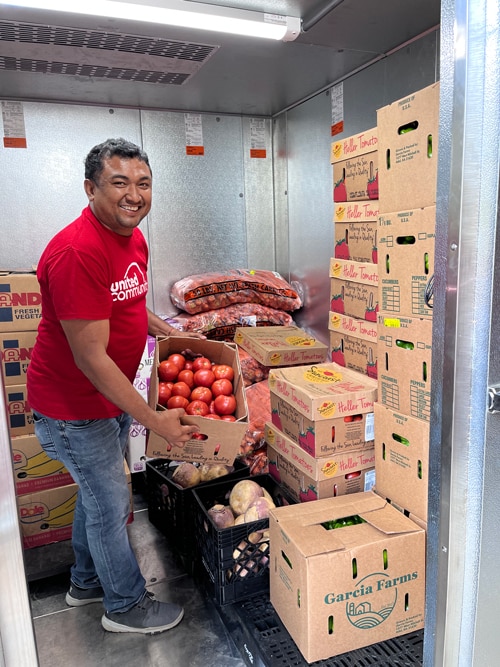 Jose stands in the new walk-in fridge, smiling and holding a box of tomatoes