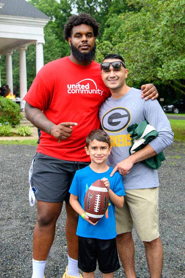 Rasheed Walker poses with a Green Bay Packers fan and his son, who's holding a football at our Family Fun Day, hosted by our Family Achievement Program