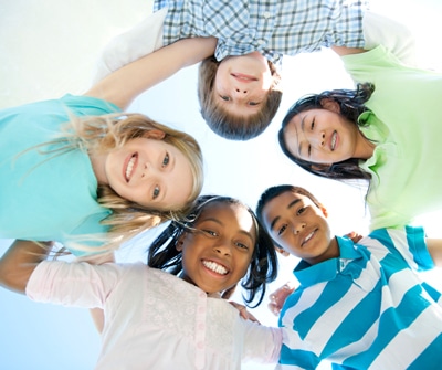 Five kids huddled together looking down and smiling on a bright, blue sky day